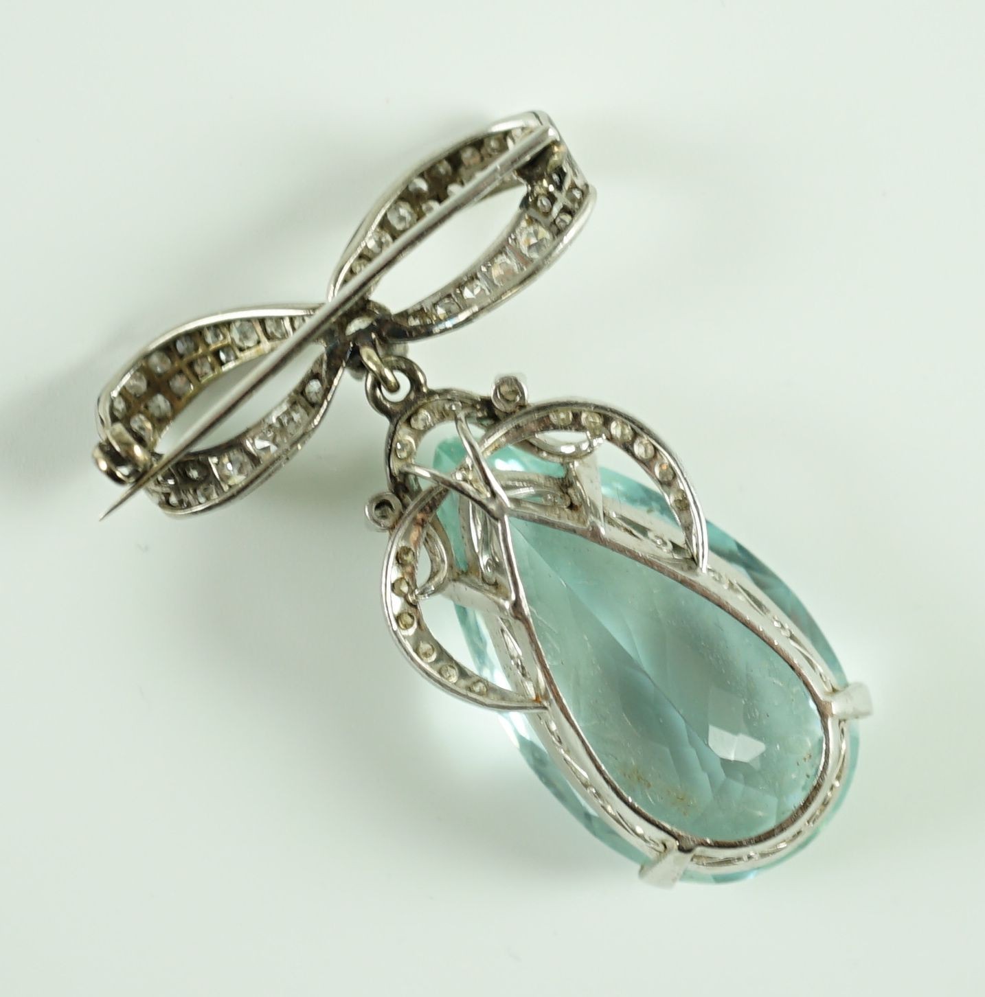 A mid 20th century continental white gold, facet cut pear shaped aquamarine and diamond set drop pendant, on a diamond set ribbon bow brooch